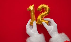 a pair of Santa hands holding up two balloons that make out 12