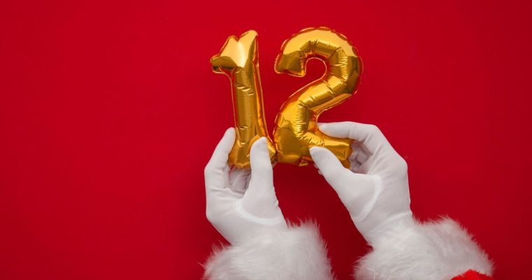 a pair of Santa hands holding up two balloons that make out 12