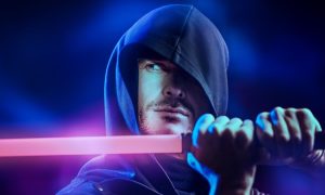 a man wearing a hooded cloak and holding a lightsaber