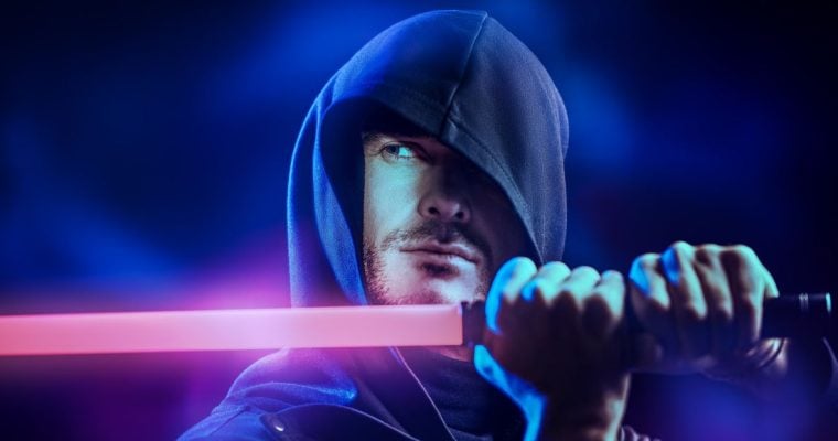 a man wearing a hooded cloak and holding a lightsaber