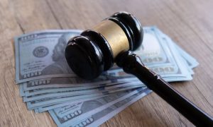 Several $100 Bills Lay on Wood Table with Gavel On Top