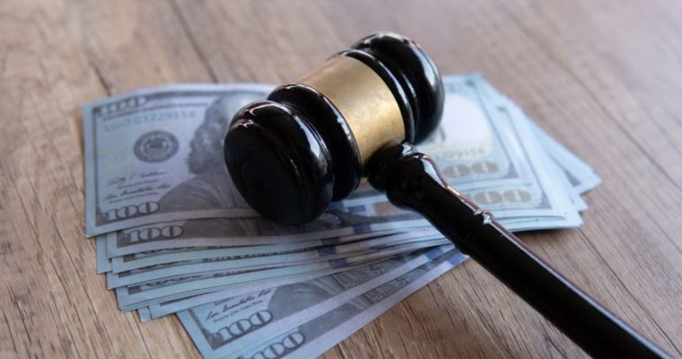 Several $100 Bills Lay on Wood Table with Gavel On Top