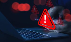 Man Holding Cell Phone Sees Red Warning Sign Above Laptop
