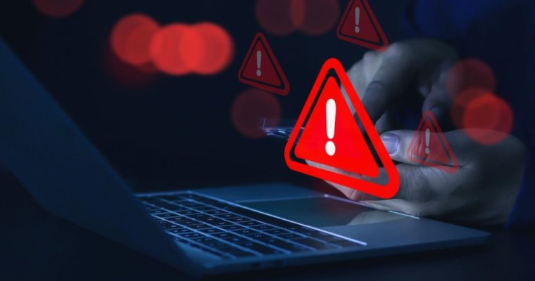 Man Holding Cell Phone Sees Red Warning Sign Above Laptop