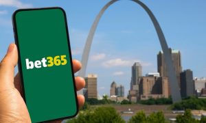 A hand holds a smartphone displaying the bet365 logo with the St. Louis Gateway Arch and downtown skyline in the background.