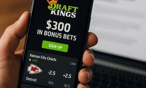 Close-up of a person holding a smartphone showing the DraftKings Sportsbook app with football and basketball images.