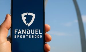 A realistic photo showing the St. Louis Gateway Arch at dusk with a smartphone displaying the FanDuel Sportsbook logo in the foreground.