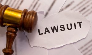 Torn Paper Reads "Lawsuit" Next To Wooden Gavel Atop Legal Papers