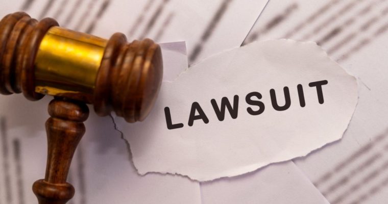 Torn Paper Reads "Lawsuit" Next To Wooden Gavel Atop Legal Papers
