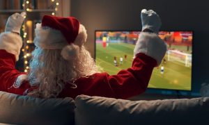 Santa Claus Watches Sports Game on TV Sitting On Couch