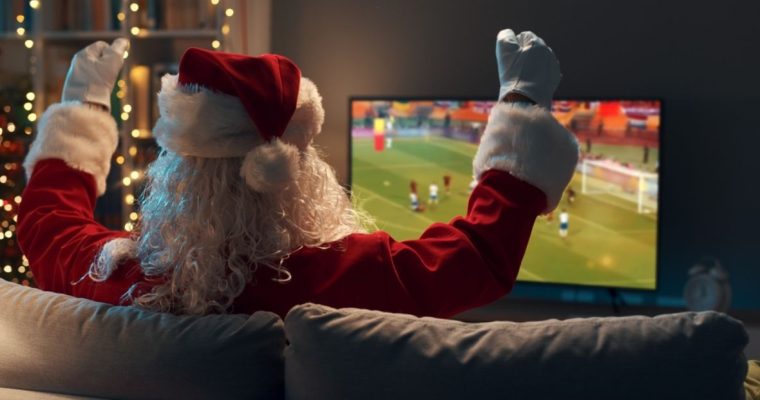 Santa Claus Watches Sports Game on TV Sitting On Couch