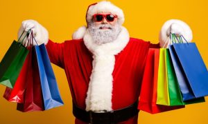 Smiling Santa Holds Up Colorful Gift Bags in Both Hands