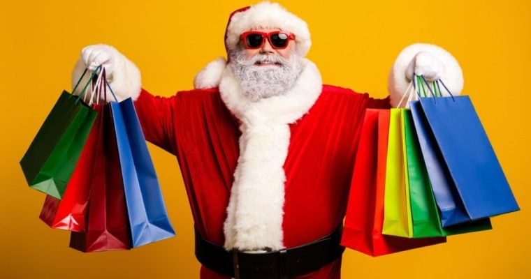 Smiling Santa Holds Up Colorful Gift Bags in Both Hands