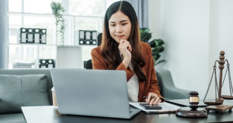 Woman Sits Thinking in Front of Computer with Gavel, Scale and Calculator on Desk