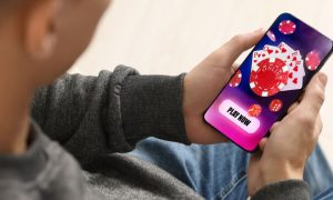 Man Sits and Holds Cell Phone Displaying Online Casino Poker Game