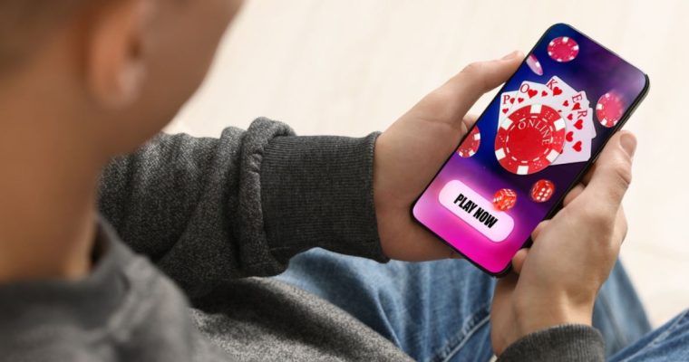 Man Sits and Holds Cell Phone Displaying Online Casino Poker Game