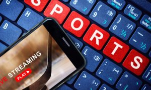 Blue Computer Keyboard Reads Sports in Red Keys with Cell Phone Streaming Hockey Game Sitting On Top