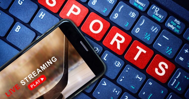 Blue Computer Keyboard Reads Sports in Red Keys with Cell Phone Streaming Hockey Game Sitting On Top