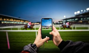 Man Holding Horse Race on Cell Phone While Sitting at Race
