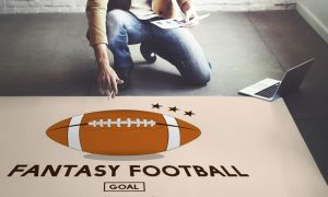 Large Fantasy Football Poster on Floor With Man Kneeling Above Holding Paper and Pen