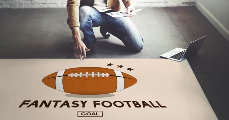 Large Fantasy Football Poster on Floor With Man Kneeling Above Holding Paper and Pen