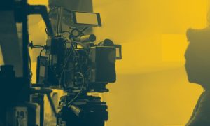 Man Observes Film Set Sitting Next to Camera in Yellow and Black Hues