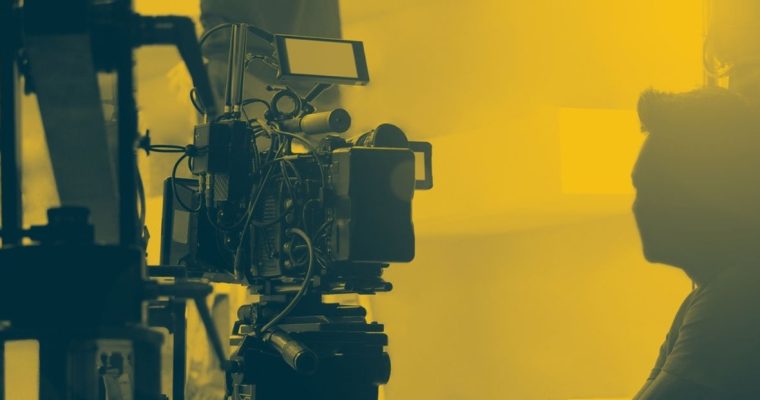 Man Observes Film Set Sitting Next to Camera in Yellow and Black Hues