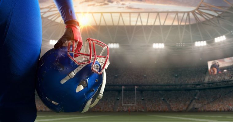 Brightly-Lit American Football Stadium with Close Up Of Player's Hand Holding Blue and Red Helmet