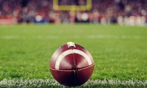 Football Sits on Green American Football Field With Field Goal in Background