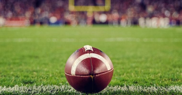 Football Sits on Green American Football Field With Field Goal in Background