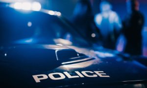 Police Car In Focus With Police Arresting a Suspect in Blurred Background