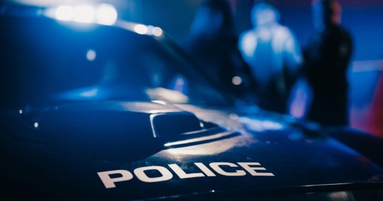 Police Car In Focus With Police Arresting a Suspect in Blurred Background