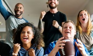 Friends Enthusiastically Watch a Football Game With One Man Holding Football