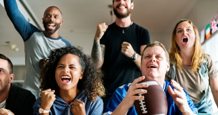Friends Enthusiastically Watch a Football Game With One Man Holding Football