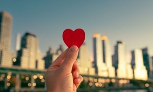 Blurry NYC Skyline As Background to Hand Holding Up Red Heart