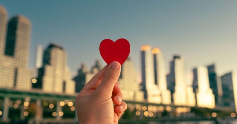 Blurry NYC Skyline As Background to Hand Holding Up Red Heart