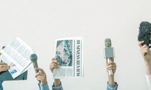 News Reporters Hold Up Microphones and Newspapers on Solid Background