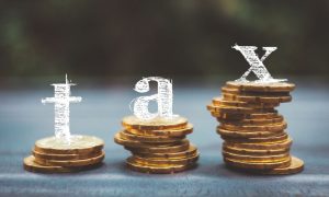 Letters T A X Sit Above Stacks of Gold Coins