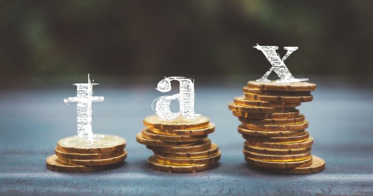 Letters T A X Sit Above Stacks of Gold Coins