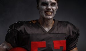 American Football Player In Zombie Makeup Wears Black Jersey with Red Numbers