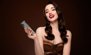 Smiling Brunette Holds Cell Phone on Brown Background