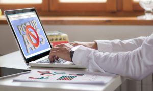 Man At Desk Works on Laptop That Shows Pop Up Ads Blocked