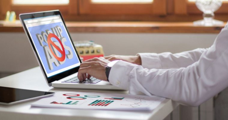 Man At Desk Works on Laptop That Shows Pop Up Ads Blocked