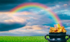 Green Grass with Full Pot of Gold and Rainbow Arching Across Cloudy Sky
