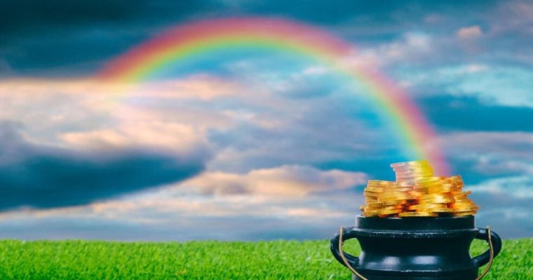 Green Grass with Full Pot of Gold and Rainbow Arching Across Cloudy Sky