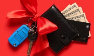 Red Bow on Car Keys Next To Black Wallet With $100 Bills Sticking Out