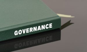 Green Book with White Letters on the Side Read Governance Sits on Metalic Desk