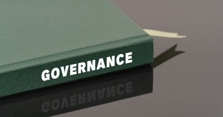 Green Book with White Letters on the Side Read Governance Sits on Metalic Desk