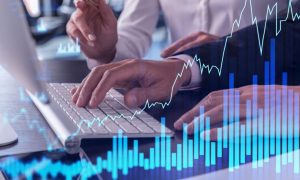 Two People Sit at Desk In Front of Computer with Digital Overlay of Line and Bar Graphs