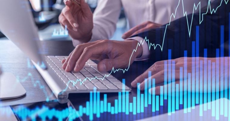 Two People Sit at Desk In Front of Computer with Digital Overlay of Line and Bar Graphs